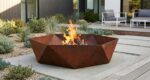 Modern hexagonal corten steel fire pit with burning wood logs in modern garden