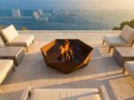 Hexagonal corten steel fire pit on luxury seaside terrace with modern outdoor furniture