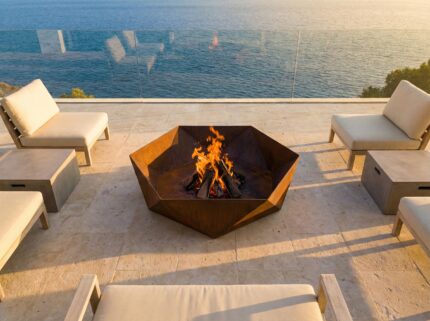 Hexagonal corten steel fire pit on luxury seaside terrace with modern outdoor furniture