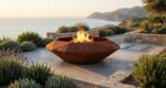 Octagonal Corten steel fire pit Diamond Octagon TOP in a coastal garden at sunset, surrounded by lavender and a stone wall.